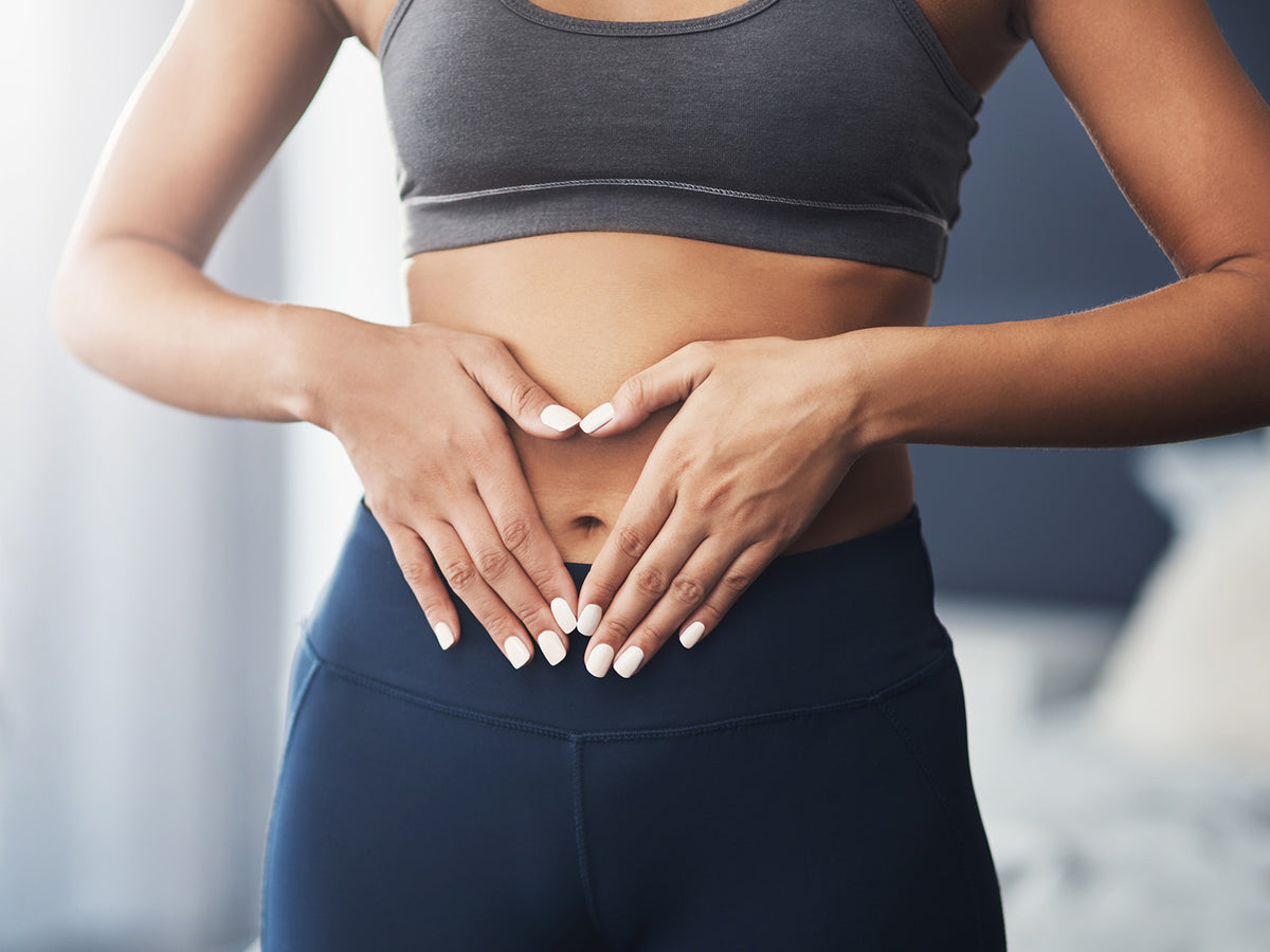 Close-up of a woman forming a heart shape over her stomach with her hands, representing digestive and gut health.